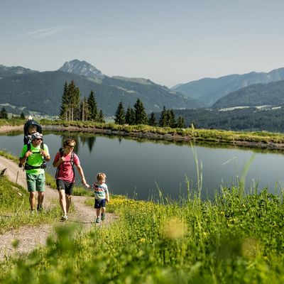 Eine Familie wandert neben einen kleinemSee entlang.